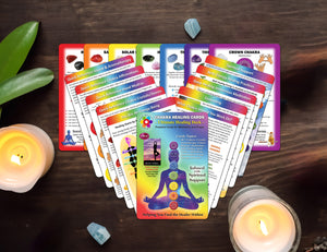 full deck of chakra healing cards spread out on a wooden table with candles, crystals and a plant.